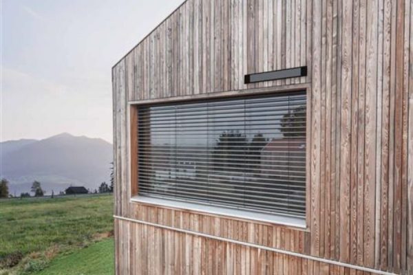 Nachhaltiges Holzhaus mit solarbetriebenem Raffstore zur effektiven Licht- und Wärmeregulierung.